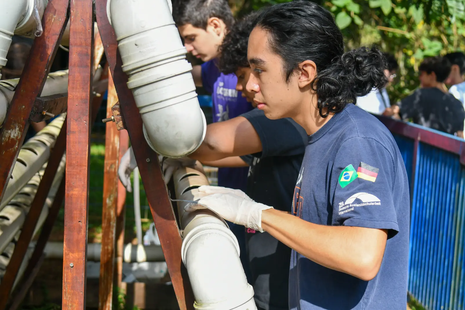 Alunos do ensino médio em um espaço aberto ao ar livre, utilizando luvas para manusear materiais