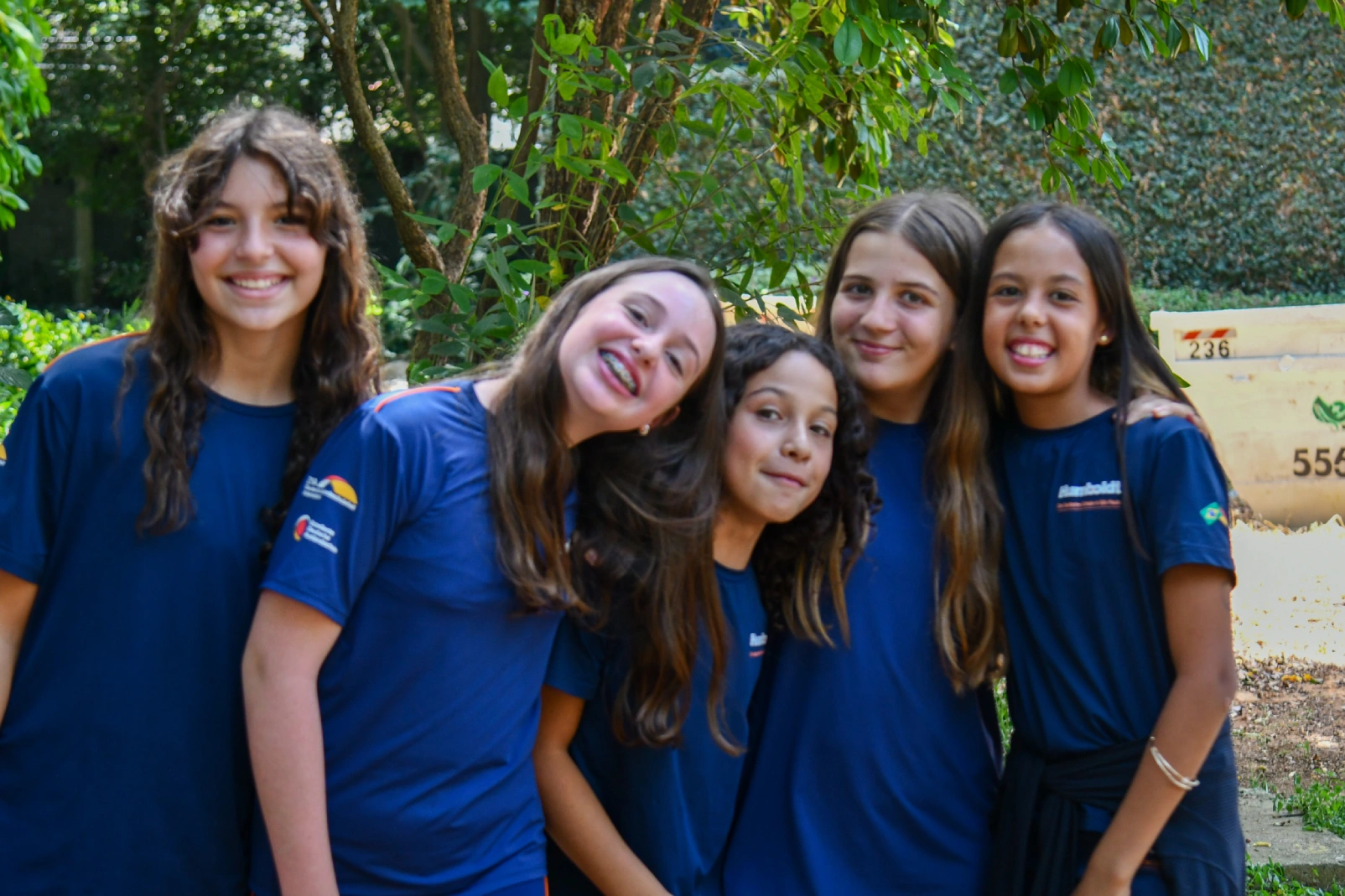 Alunas do fundamental 2 abraçadas em um espaço verde aberto